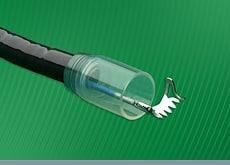 A black endoscope with the flexible mega cap attached at the distal end. The grasper is pushed through the working channel, grabbing a metallic clip piece.